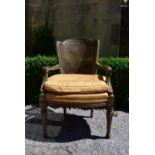 A Continental style painted and caned back armchair with fitted squab cushion raised on shaped