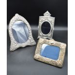 An arched silver floral embossed easel mirror and two other silver embossed mirrors each bearing