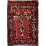 A prayer rug with central pole medallions on a deep red field contained by stylised multiple