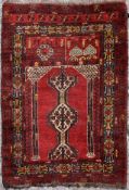 A prayer rug with central pole medallions on a deep red field contained by stylised multiple