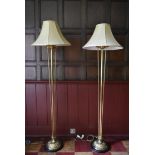 A pair of heavy brass standard lamps with floral decoration and matching shades standing on ebonised