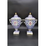 A pair of lidded Dresden urns with gilt finials and blue and gold lattice work glaze with painted