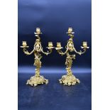 A pair of gilt metal three branch table candelabras with cherub surmounts raised on Rococo scrolling