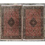 A pair of silk Persian rugs with central floral pole medallion on a madder ground with scrolling