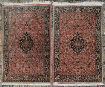 A pair of silk Persian rugs with central floral pole medallion on a madder ground with scrolling