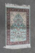 A silk rug with scrolling foliate design on a powder blue field contained by naturalistic floral