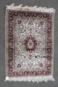 A Persian style silk rug with floral medallion and spandrels on a fawn ground contained by scrolling