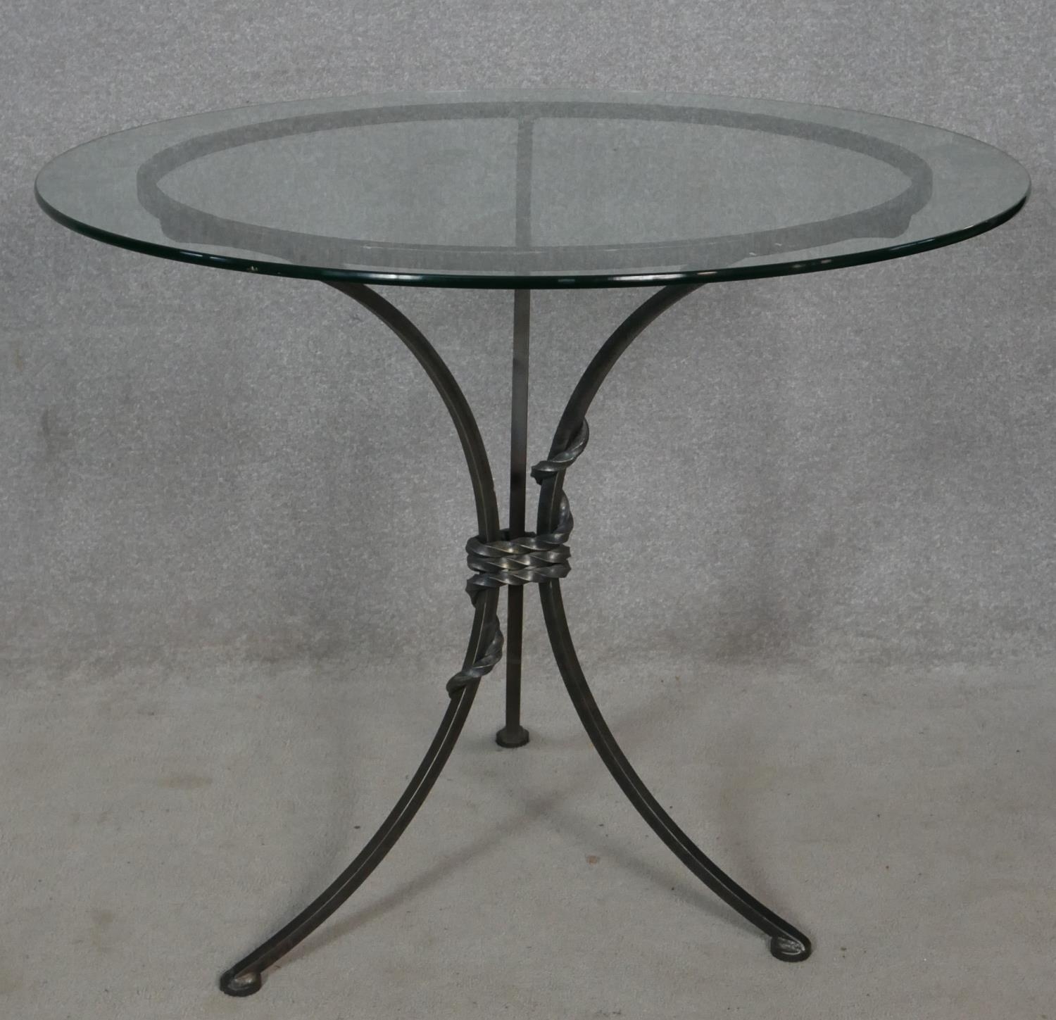A plate glass topped conservatory table on wrought metal tripod base. H.78 D.91.5cm