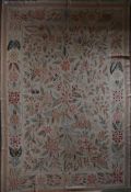 A needlepoint carpet with profuse flower and leaf design across the beige ground contained by floral