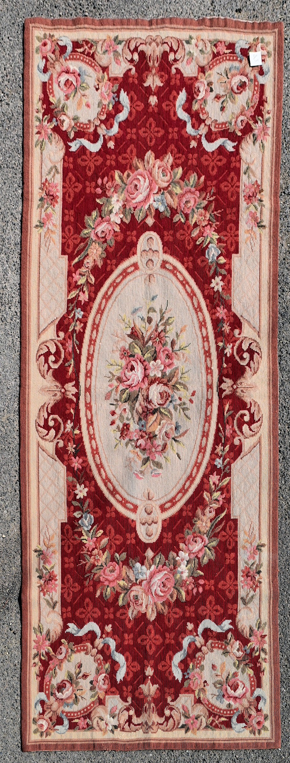 A needlepoint rug with central floral cartouche on a burgundy field within ribbon and flowerhead