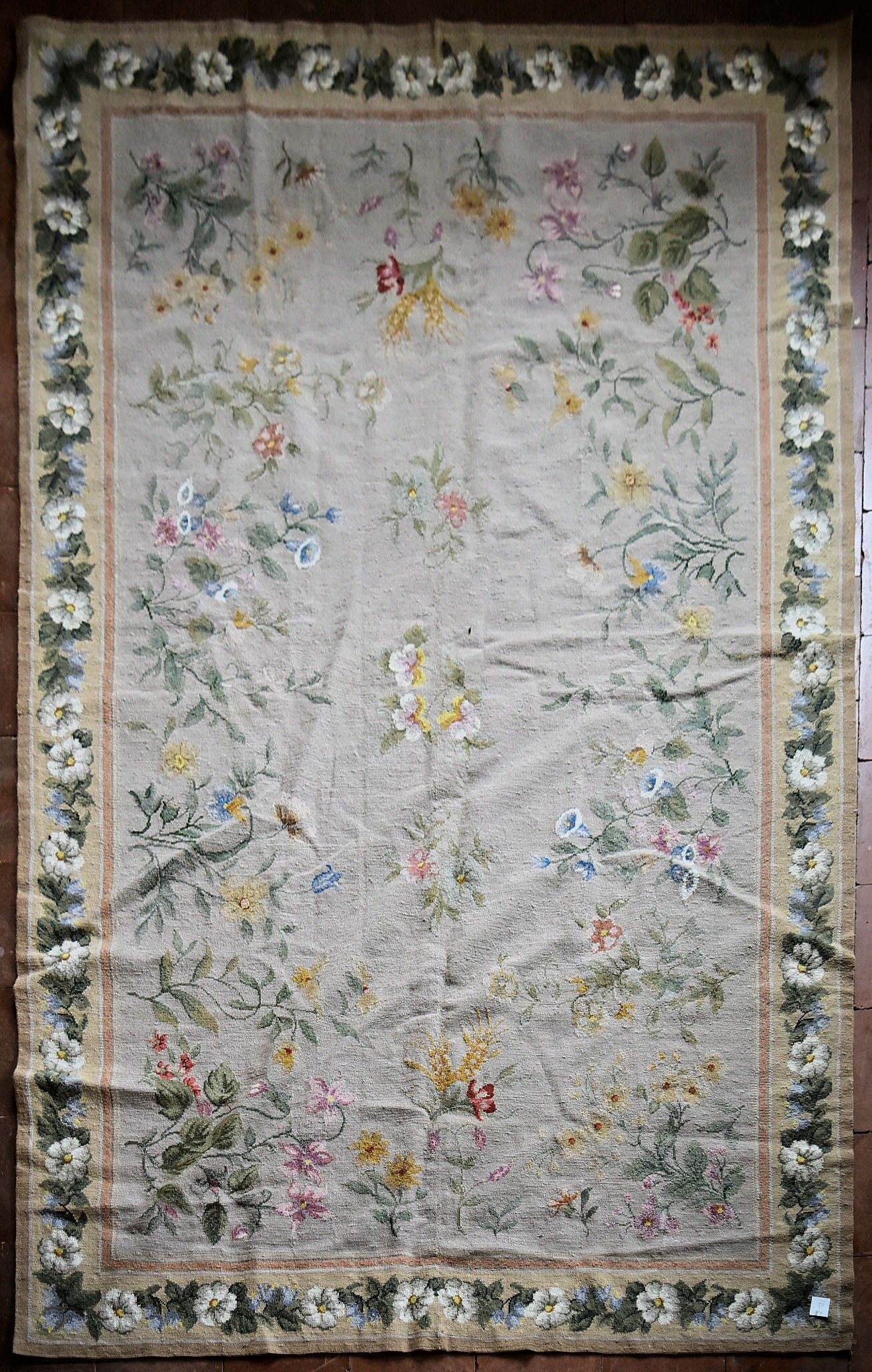A needlepoint rug with foliate and wild flower sprays across a fawn field contained by garlands of