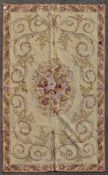 A needlepoint rug with central floral spray and scrolling foliage on a biscuit ground within leaf
