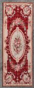 A needlepoint rug with central floral cartouche on a burgundy field within ribbon and flowerhead