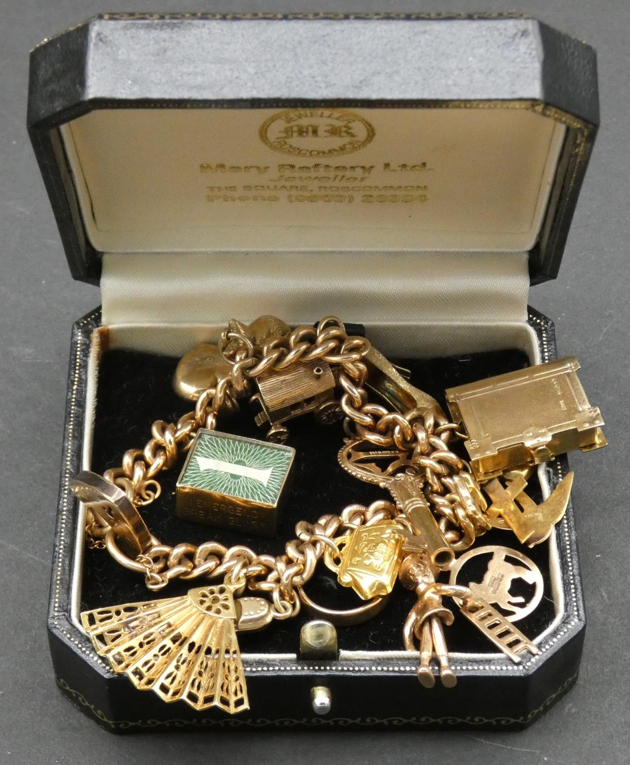 A vintage solid curb link 9ct gold charm bracelet with fifteen 9ct yellow gold charms. The charms