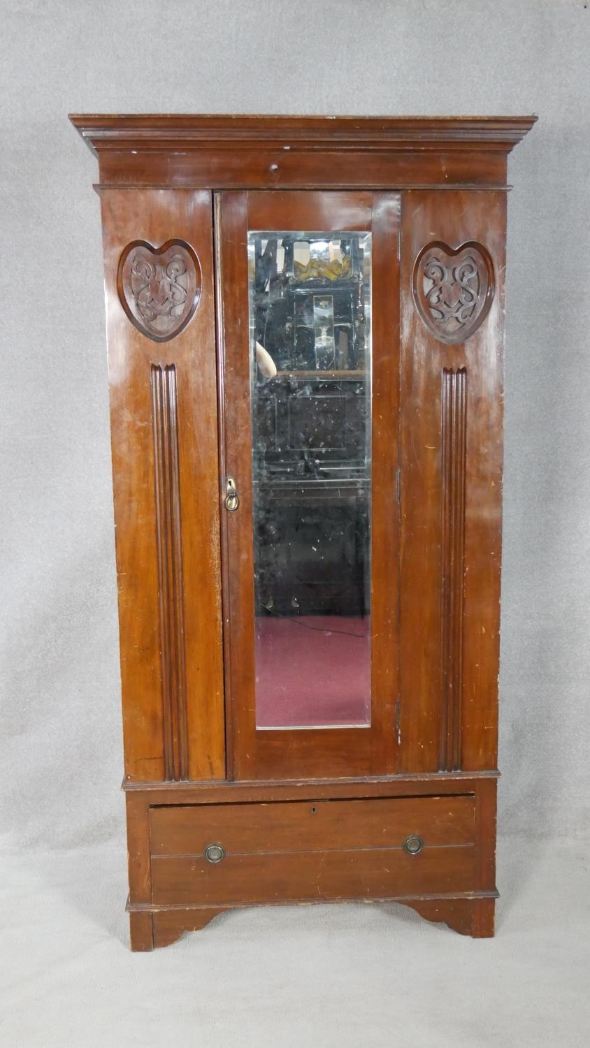 A late Victorian carved walnut wardrobe with bevelled mirrored door enclosing hanging space above