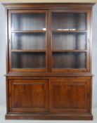 An oak library bookcase with glazed sliding doors enclosing bookshelves above sliding panel doors on