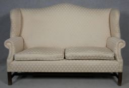 A Georgian style mahogany framed wing back two seater sofa in diamond pattern ivory upholstery on