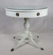 A vintage white painted drum table with plate glass top and frieze drawers raised on pedestal base