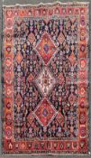 A Persian Kashkai rug with triple hooked medallions on a midnight ground within a stylised multi