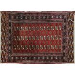 A Bokhara style rug with repeating gul motifs on a madder ground contained within stylised