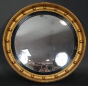 A Regency style gilt convex wall mirror with tied ribbon and ball detail in an ebonised reeded slip.