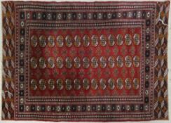 A Bokhara style rug with repeating gul motifs on a madder ground contained within stylised