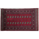 A Bokhara rug with repeating gul motifs on a deep red ground within stylised floral multiple