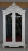 A Louis XV style painted armoire with Rococo carved pediment above a pair of bevelled glass doors on