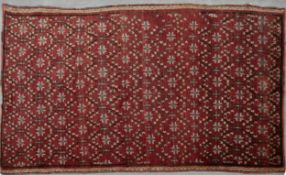 An Eastern rug with repeating floral motifs on a burgundy ground with a chevron border. L.260 W.