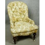 A Victorian beech framed nursing chair in deep buttoned floral upholstery on turned tapering