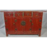 A Chinese lacquered and brass bound sideboard with four frieze drawers above four panel doors on