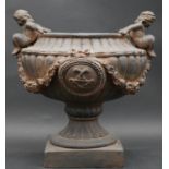 A moulded garden urn with twin cherub handles and reeded sides with swag decoration on plinth