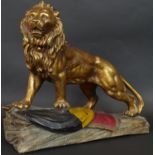 A gold and polychrome glazed ceramic sculpture of a lion roaring and standing on the Belgian flag on