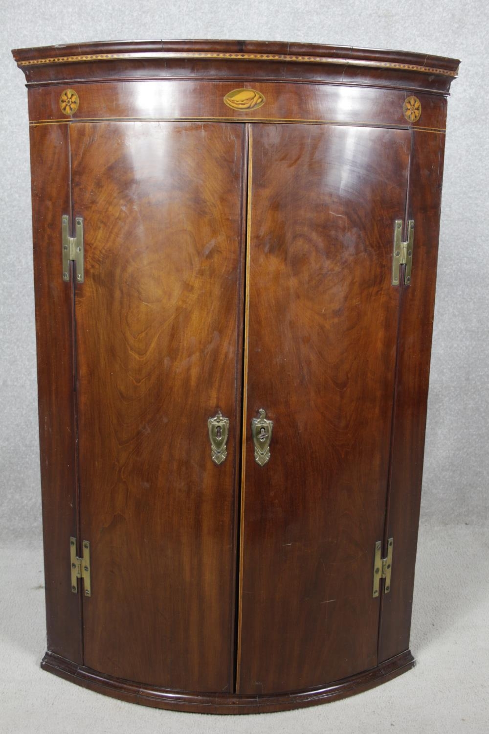 A Georgian figured mahogany bowfronted corner cupboard with satinwood and olivewood conch and floral