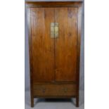 A Lombok teak hall cupboard with panel doors enclosing shelves above base drawer on block