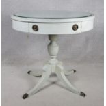 A vintage white painted drum table with plate glass top and frieze drawers raised on pedestal base