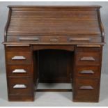 A late 19th century oak roll top desk with tambour shutter revealing fitted interior on twin