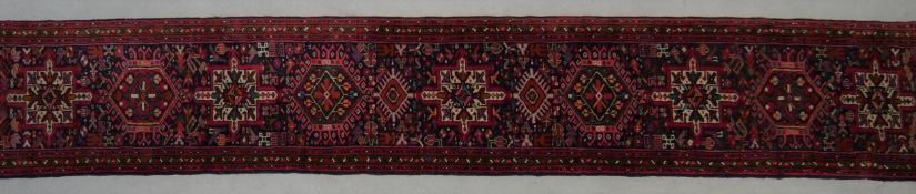 A Kazak runner with repeating hooked medallions on a midnight ground contained within stylised