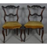 A pair of late 19th century mahogany dining chairs with carved and shaped back rails on cabriole