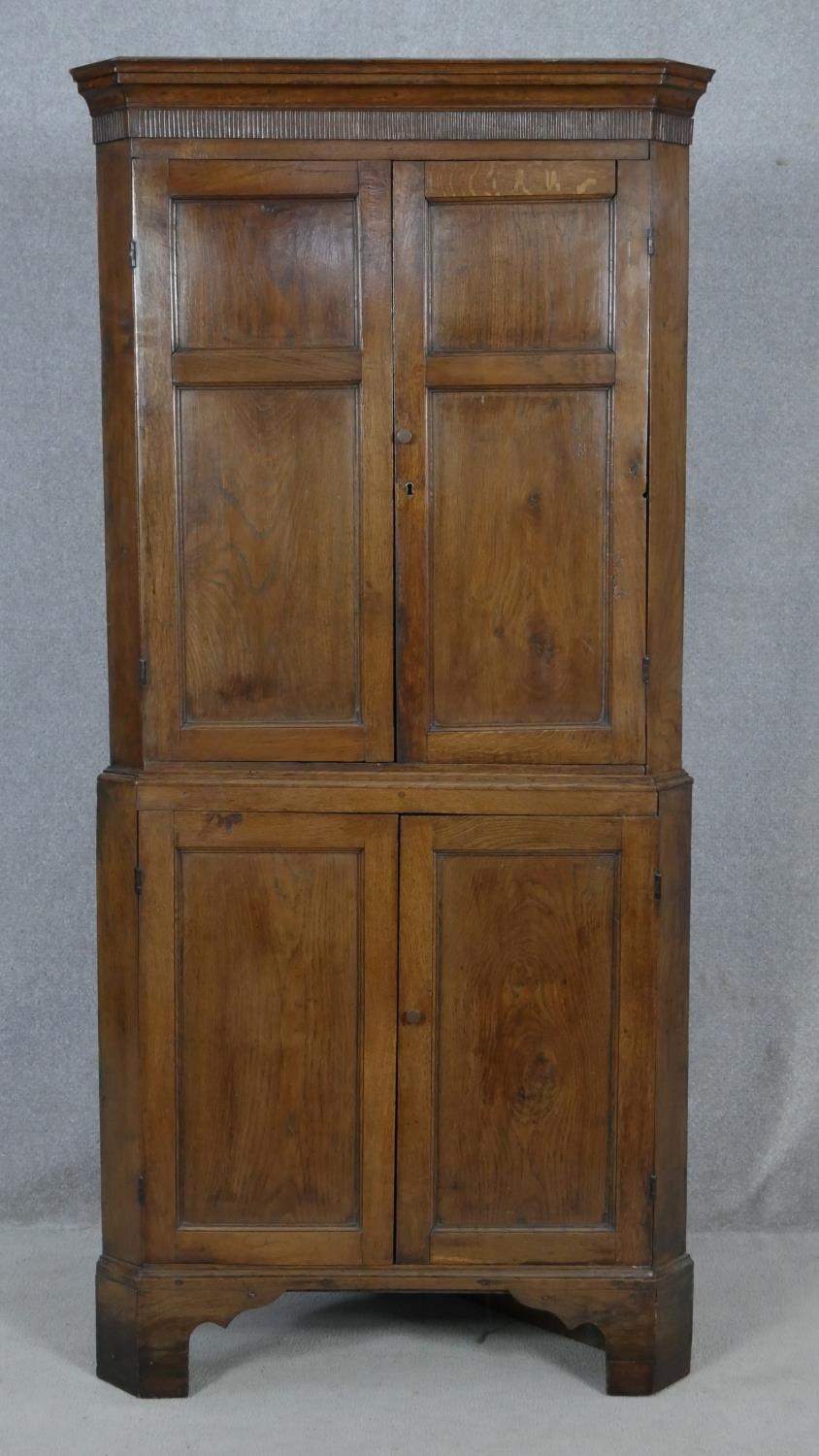 A Georgian oak two section corner cupboard with panel doors enclosing shelves on shaped bracket