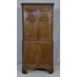 A Georgian oak two section corner cupboard with panel doors enclosing shelves on shaped bracket