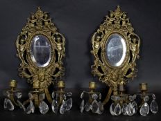 A pair of pierced brass girandoles with bevelled plates, cherub and mask detail and triple scrolling
