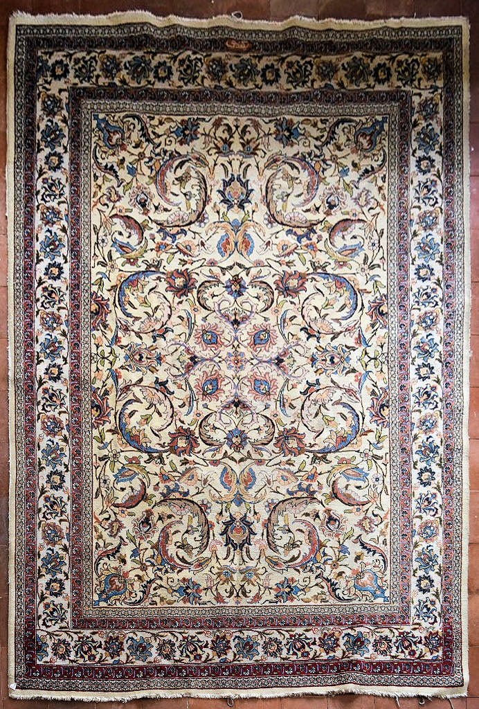 An old Persian Tabriz carpet with a repeating scrolling foliate design on a cream field within