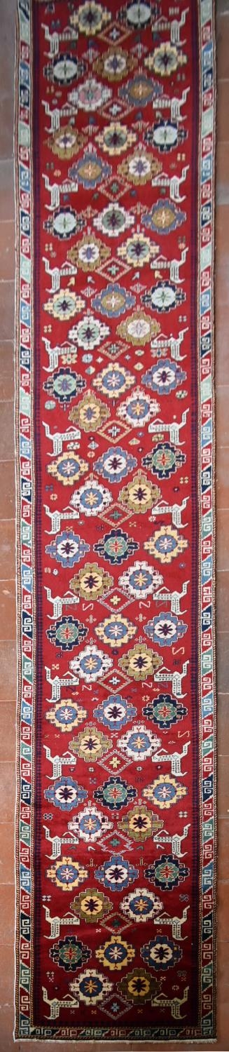 A Kazak design runner with stylised flowerhead and animal motifs across the madder ground within