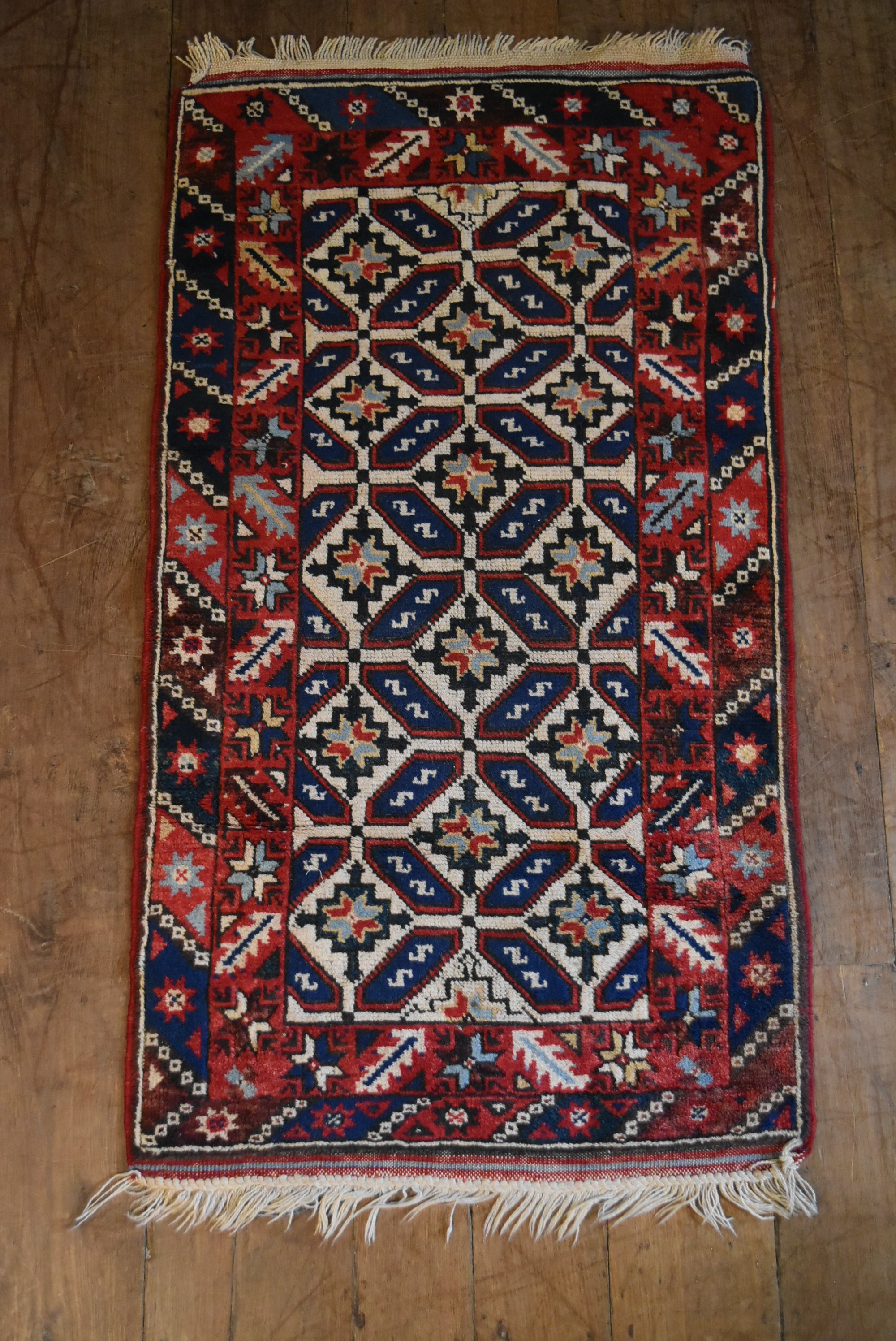 A Kazak rug with repeating stylised flowerhead motifs across the field contained by serrated palm