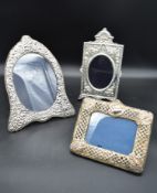 An arched silver floral embossed easel mirror and two other silver embossed mirrors each bearing