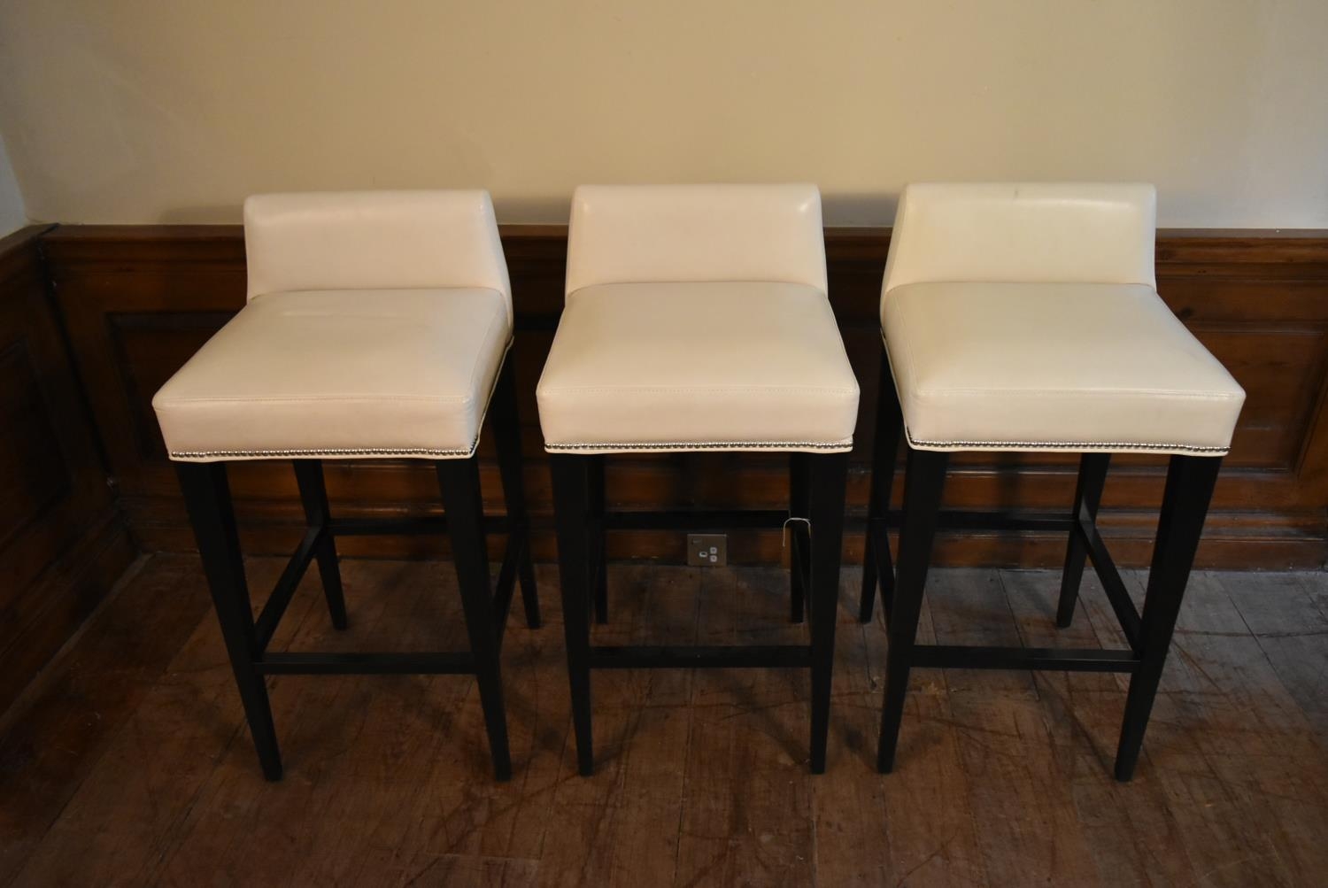 A set of three contemporary bar stools in studded ivory upholstery on square tapering stretchered