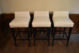 A set of three contemporary bar stools in studded ivory upholstery on square tapering stretchered