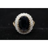 A yellow metal (tested as 9ct gold) sapphire and diamond cluster ring, set to centre with an oval