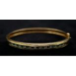 An 18 carat yellow gold, emerald and diamond bangle. Set with thirteen round mixed cut emeralds with